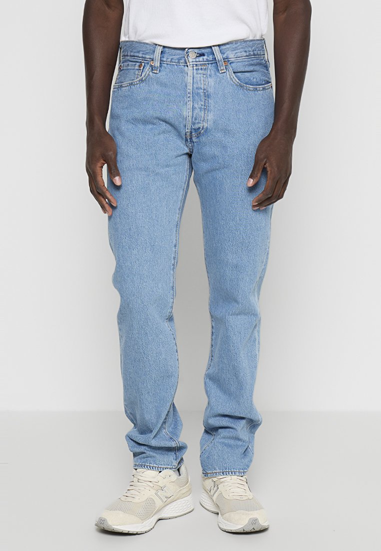 Jeans de mezclilla azul claro con un corte de pierna recta, diseño de cinco bolsillos y detalles de costura sutil. Combinados con zapatillas de colores neutros.