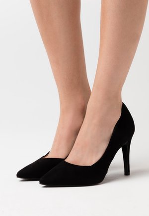 Escarpins noirs en daim à talons hauts avec un bout pointu, un décolleté bas et un talon stiletto fin, présentant une texture lisse et un design classique.