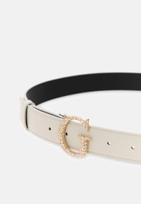 Weißer Leder-Gürtel mit schwarzem Innenfutter, ausgestattet mit einer goldfarbenen G-förmigen Schließe, die mit Strasssteinen verziert ist. Drei sichtbare Verstelllöcher.