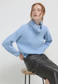 Hellblauer, gerippter Strickrollkragenpullover mit langen Ärmeln, kombiniert mit einem schwarzen Lederrock. Die Textur ist weich und entspannt.