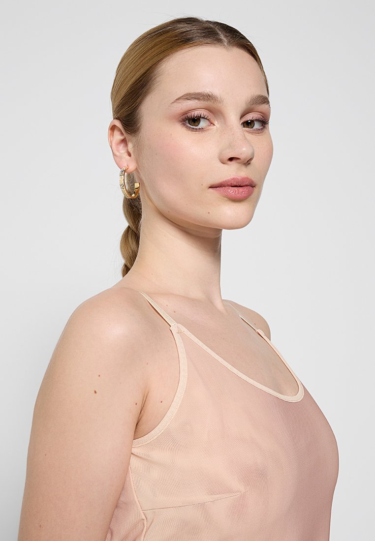 Camisón de melocotón semitransparente con tirantes finos, textura suave y diseño ajustado. Modelo vistiendo aretes de aro dorados y un maquillaje minimalista.