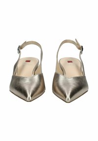 Chaussures slingback métalliques dorées avec un bout pointu, une semelle plate et une petite boucle noire sur la sangle de la cheville ; texture lisse.