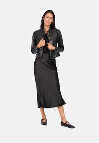 Black leather cropped jacket with gold hardware, paired with a black satin midi dress and black flats featuring a strap detail.