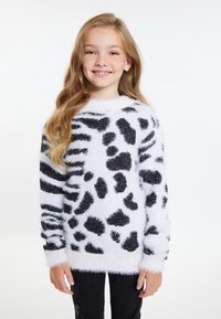 Maglione bianco morbido con macchie e strisce astratte nere, dotato di collo rotondo e texture soffice, abbinato a pantaloni neri.
