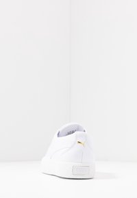 Weiße Leder-Sneaker mit strukturiertem Gummisohle, goldfarbenem Logo-Akzent und glatter Oberfläche. Der Blick von hinten hebt den gepolsterten Kragen und das klare Design hervor.