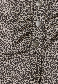 Leopardmönstrad tyg med svarta fläckar på en beige bakgrund, med tre silverknappar märkta "Street One" längs den främre sömmen.