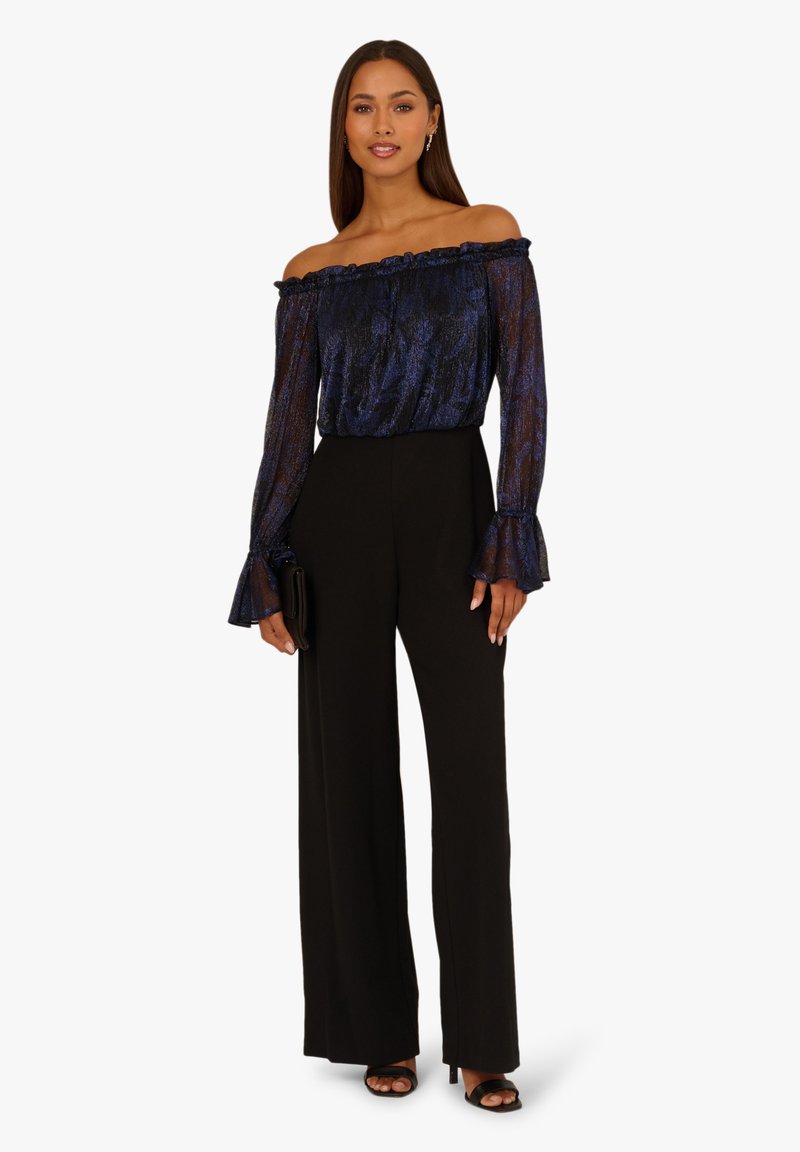 Bluzka bez rękawów w granatowym kolorze z wzorem, z falbaną przy dekolcie i szerokimi rękawami, w zestawieniu z wysokim stanem czarnymi spodniami o szerokich nogawkach.