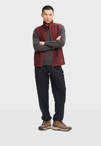 Burgundy lynlåsvest over en grå sweater, parret med mørke cargo bukser og brune vandrestøvler; glat stof, afslappet pasform, praktisk design.