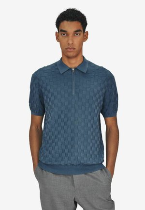 Strukturiertes kurzärmeliges Poloshirt in Dunkelblau mit gewebtem Muster, Reißverschluss sowie geripptem Saum und Kragen. Kombiniert mit hellgrauer Hose.