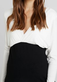 Schwarz-weißes Langarm-Oberteil mit Wickel-Bustier; weicher Stoff; gerafftes Material an der Taille; Kontrast zwischen dem weißen oberen und dem schwarzen unteren Teil.