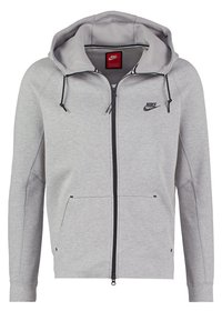 Lichtgrijze Nike hoodie met rits, zwarte trekkoorden, voorzakken en een klein zwart Nike-logo op de linkerborst.