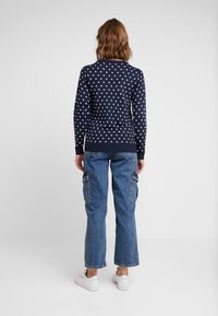 Pull en maille bleu marine à pois avec des poignets et un ourlet côtelés, associé à un jean cargo bleu clair et des baskets blanches, vu de dos.