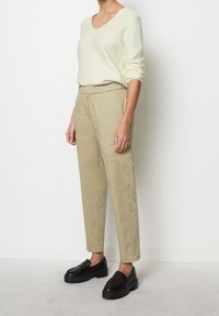Lichtcrème v-hals trui gecombineerd met beige lichte, taps toelopende broeken, voorzien van een elastische tailleband en zijzakken. Zwarte chunky loafers.