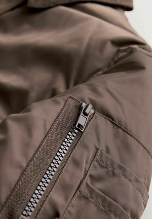 Hnědá izolační bunda s hladkou texturou, zapínáním na zip a nášivkovou kapsou na rukávu se šicími akcenty.