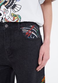 Černé džíny z denimu s vypasovaným pasem, které mají barevné potištěné podšívky kapes a živý vyšitý detail na boku.