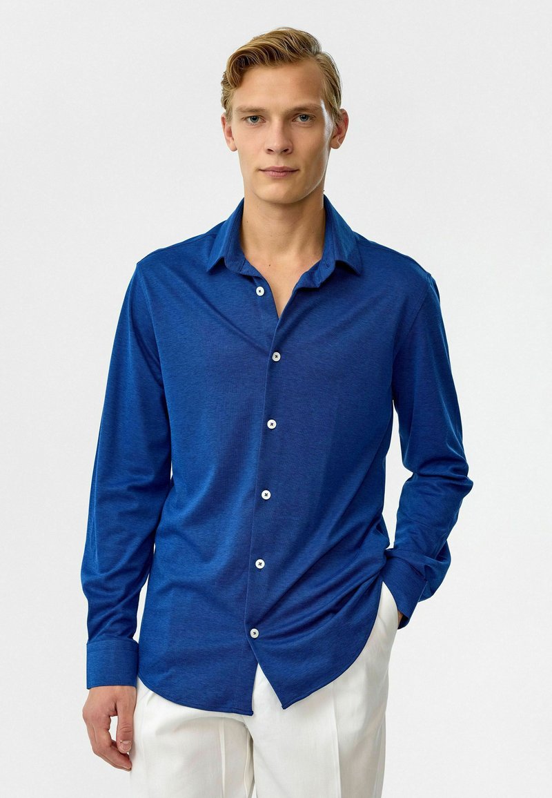 Blauwe lange mouwen shirt gemaakt van zachte stof, met een puntkraag en witte knopen, een gebogen zoom en een relaxte pasvorm.