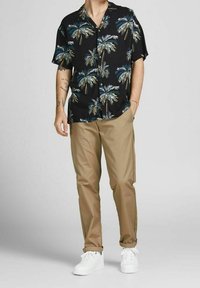 Korte mouwen zwarte shirt met palmboomprint, gecombineerd met beige broek en witte sneakers. Het shirt heeft een relaxte pasvorm en een knoopsluiting.