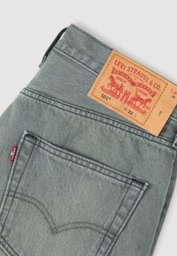 Γκρι τζιν Levi's διπλωμένο για να φαίνεται η πίσω τσέπη, η κόκκινη ετικέτα Levi's και το ταμπά δερμάτινο λογότυπο με λεπτομέρειες μεγέθους.