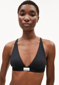 Soutien-gorge noir côtelé avec un design en v profond. Présente une étiquette logo au centre devant et des bretelles fines. Tissu doux et extensible.
