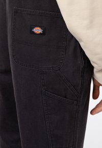 Svarta arbetsbyxor i slitstarkt tyg, med en sidoficka som har en framträdande Dickies-logotyppatch och detaljerade sömnadsdetaljer.