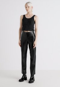 Top scurt negru, asortat cu pantaloni din piele ecologică neagră, cu talie înaltă, și cizme negre cu toc gros. Textură netedă cu un design ajustat.