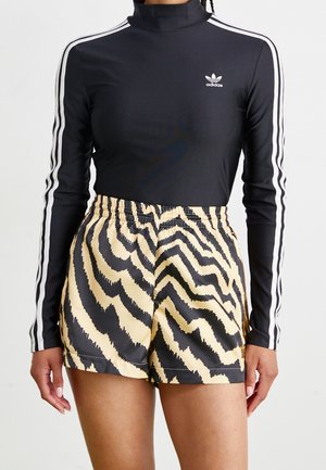 Černý top Adidas s dlouhým rukávem s bílými pruhy, nošený s vysoce pasovanými béžovo-černými šortkami se vzorem zebry na osobě.