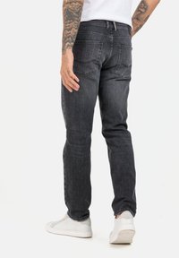 Dunkelgraue Jeans im Slim-Fit-Stil mit mittelhohem Bund, gesteppten Gesäßtaschen und leichtem Verblassen. Kombiniert mit weißen Sneakers.