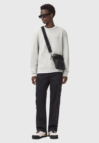 Felpa grigia chiara, pantaloni cargo neri, borsa a tracolla nera e occhiali da sole neri. Le calzature presentano una miscela di tonalità crema e scure.