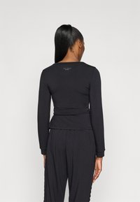 Top negru cu maneci lungi, guler rotund și detalii plisate la spate. Fabricat dintr-un material neted; prezintă un branding subtil pe partea superioară a spatelui.