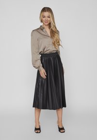 Beige samettibluse med en strukturerad krage, ihop med en plisserad svart fusk läderkjol. Öppen tå svarta klackskor fulländar outfiten.