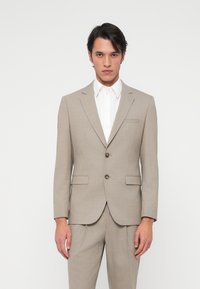 Ανοιχτό μπεζ κοστούμι με υφαντική υφή, μονόχρωμο σχέδιο και δύο κουμπιά. Συνδυάζεται με κλασικό λευκό πουκάμισο. Ραμμένο για τέλεια εφαρμογή.