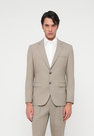 Completo beige chiaro con una trama testurizzata, design a un solo petto e due bottoni. Abbinato a una classica camicia bianca. Vestibilità su misura.