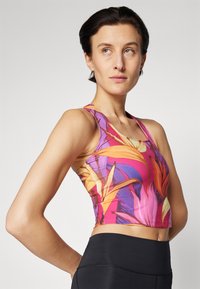 Crop top de sport avec un motif floral vif, présentant des couleurs rose, orange et violet. Fabriqué en matériau extensible avec un design ajusté.