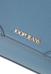 Borsa a tracolla in pelle blu tessurizzata con il logo dorato "JOOP! JEANS". Presenta dettagli di cucitura e un design slim.