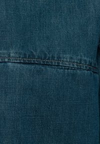 Tela de mezclilla azul con una textura suave y un detalle de costura mínimo. Presenta un sutil patrón de tejido uniforme.