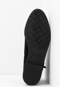 Chaussure en daim noir avec une semelle en caoutchouc texturée présentant un motif floral. Comprend un logo de marque embossé et la taille sur la semelle.