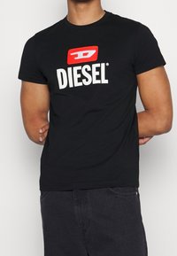 Svart kortärmad t-shirt i bomull med en röd och vit "DIESEL"-logotyp på framsidan. Standard design med rund halsringning.