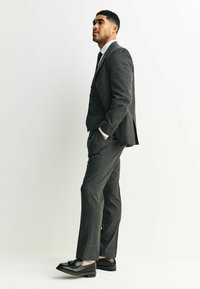 Traje gris a medida con un acabado texturizado, combinado con una camisa blanca y una corbata de estampado. Mocasines negros completan el look formal.