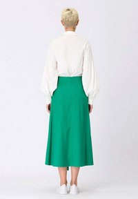 Chemise blanche à manches longues avec des manches bouffantes, associée à une jupe midi plissée verte. Comprend une fermeture éclair au dos et des baskets blanches.