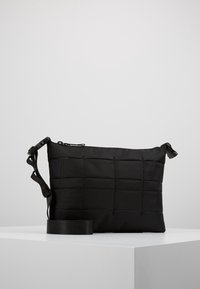 Borsa crossbody nera realizzata in tessuto testurizzato con un design trapuntato. Presenta una chiusura con zip e una tracolla regolabile. Forma compatta e rettangolare.