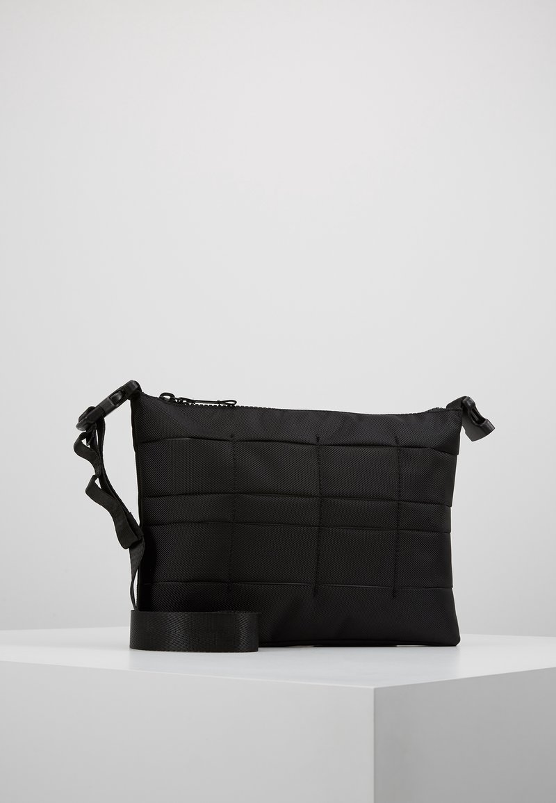Borsa crossbody nera realizzata in tessuto testurizzato con un design trapuntato. Presenta una chiusura con zip e una tracolla regolabile. Forma compatta e rettangolare.