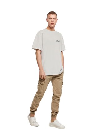 Lys grå oversized t-skjorte med korte ermer, med en liten svart grafikk. Kombinert med beige cargobukser og hvite sneakers.