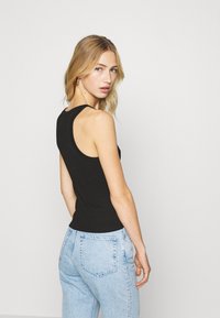 Top de alças preto com decote redondo, design justo e alças largas, combinado com jeans de cintura alta azul claro.