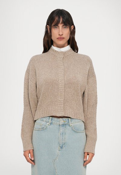 Beige cropped trui met een hoge hals, geribde manchetten en een textuurpatroon. Gecombineerd met een lichtblauwe denimrok.