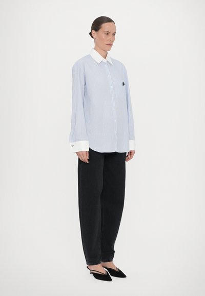 Blue and white striped shirt with a white collar, a single chest pocket, and decorative black logo. Paired with black wide-leg pants and heels.