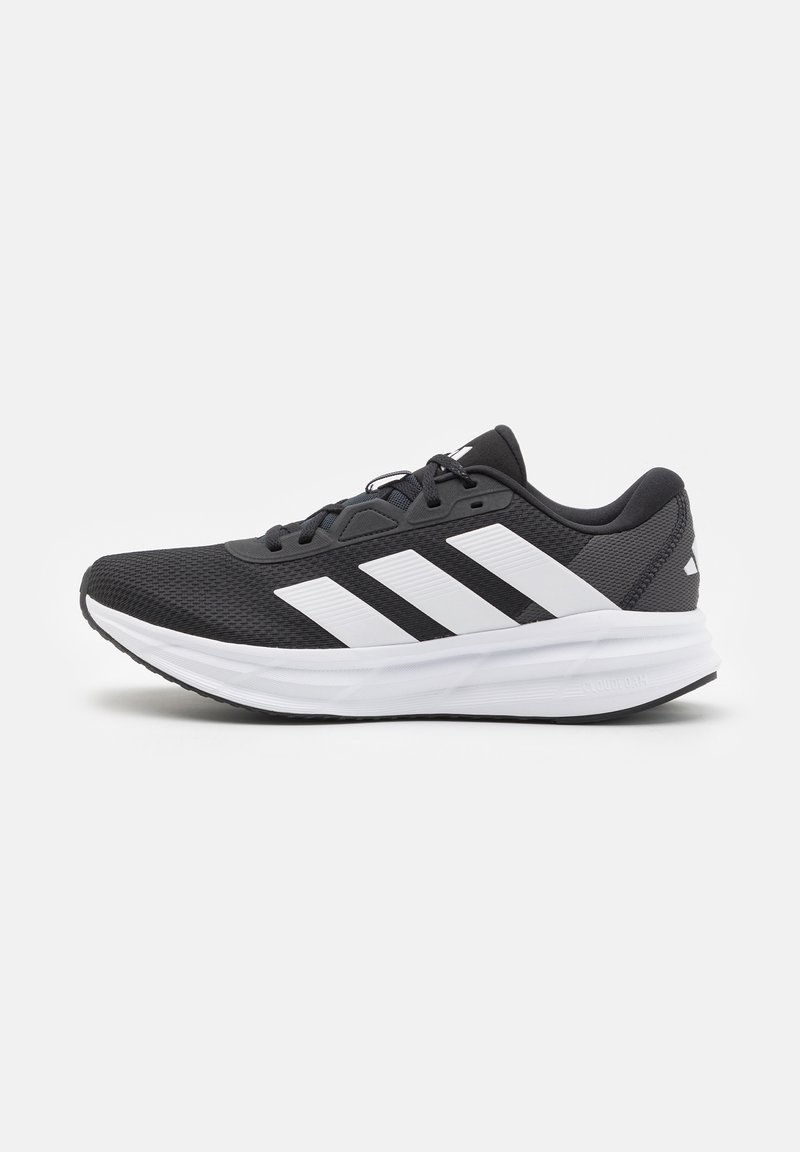 Chaussure de course Adidas noire et blanche avec trois bandes blanches sur le côté et une semelle blanche amortissante sur fond uni.