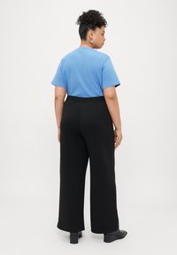 Kék pamut póló, rövid ujjakkal, fekete, bő szárú nadrággal párosítva, rugalmas derékrésszel és sima textúrával, fekete bokacsizmával viselve.