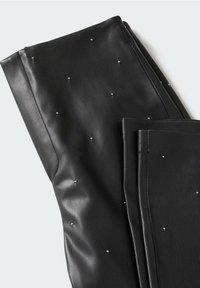Pantalon noir en similicuir avec une texture lisse et une finition brillante, orné de petits clous argentés pour l'accent. Plié proprement.