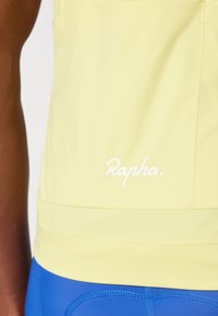 Personne portant un maillot de cyclisme Rapha jaune clair et un short de cyclisme rembourré bleu, visibles de la taille jusqu'à mi-cuisse.