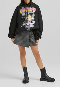 Musta huppari, jossa värikäs "Boruto"-kuvio, yhdistetty harmaaseen raidalliseen minihameeseen, jossa on nyöritystyyppiset yksityiskohdat, sekä mustiin nilkkureihin.